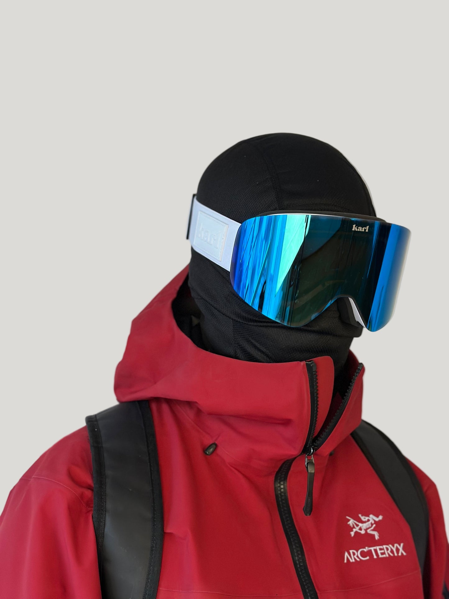 Person wearing a red jacket with Arc'teryx logo, black helmet, and blue goggles against a plain background