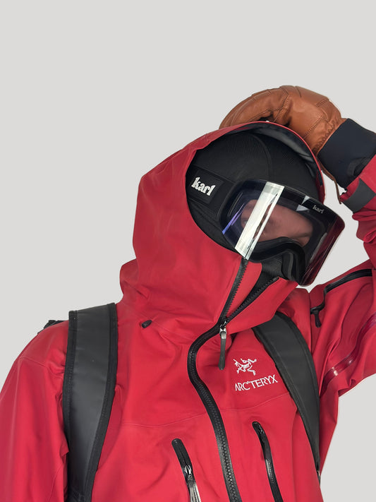 Person wearing a red jacket with a helmet and goggles, featuring Arc'teryx branding.