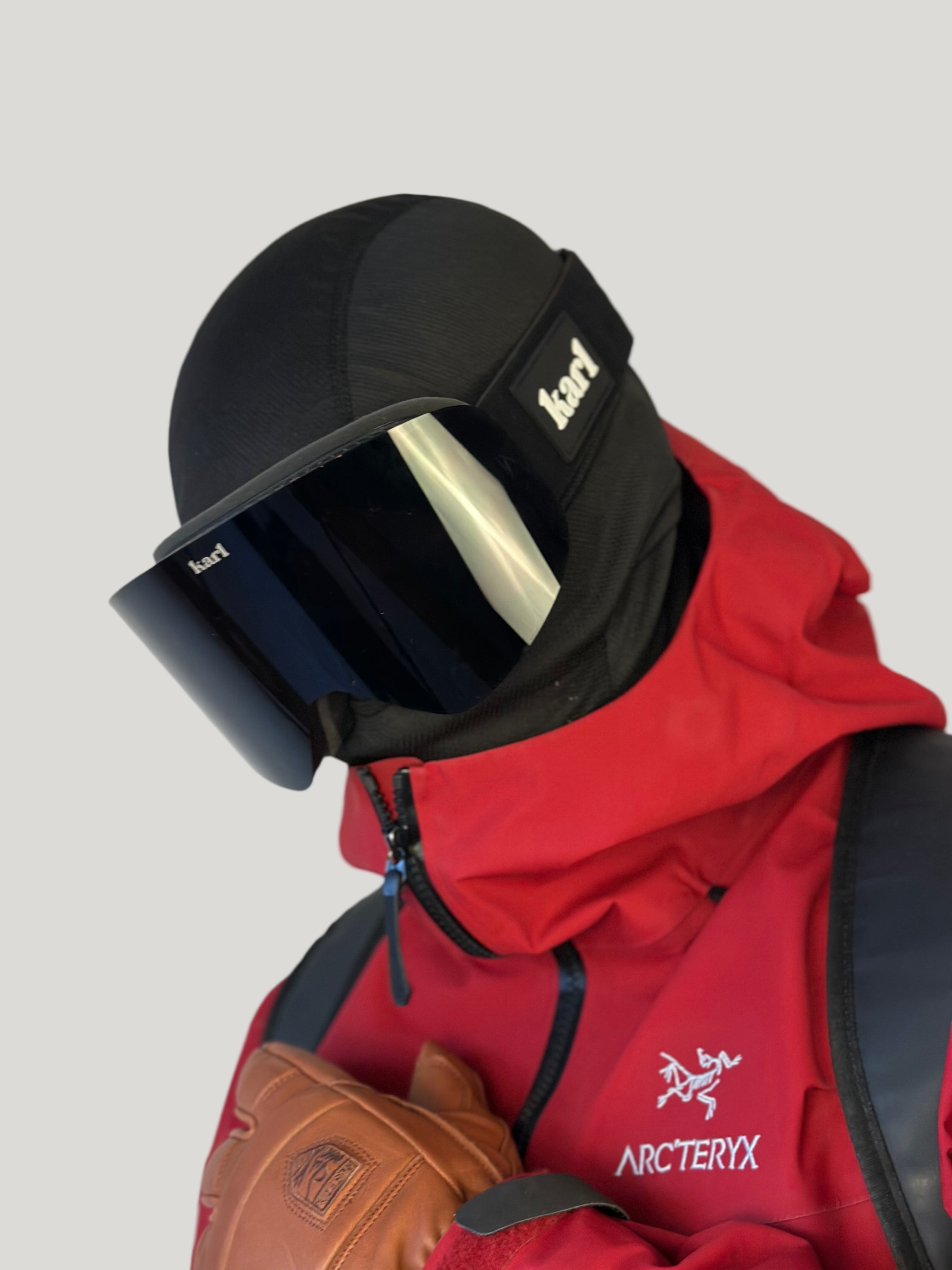 Person wearing a black helmet with a ski goggles and a red Arc'teryx jacket against a white background