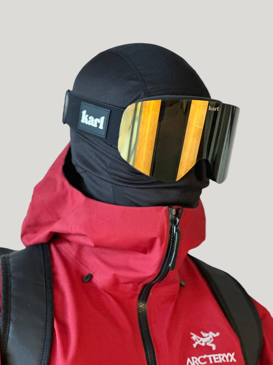 Person wearing a red Arc'teryx jacket and black skigoggles with gold lens