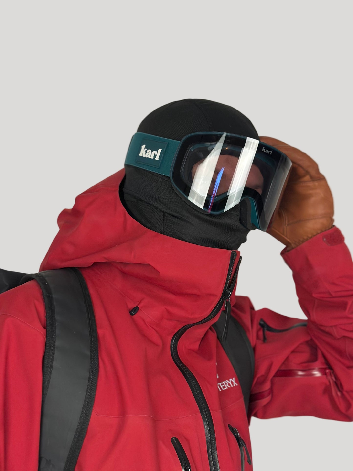 Person wearing a red jacket and black goggles with Karl branding, holding goggles.