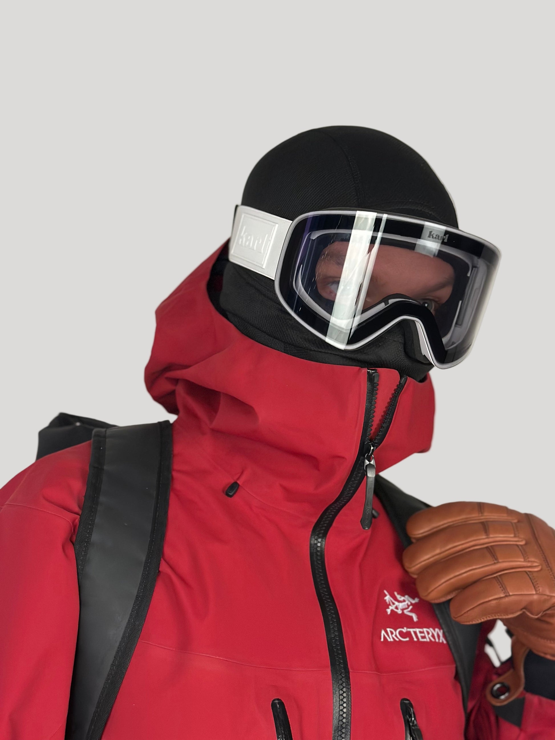 Person wearing a red jacket, black helmet with white goggles, and brown gloves on a plain background