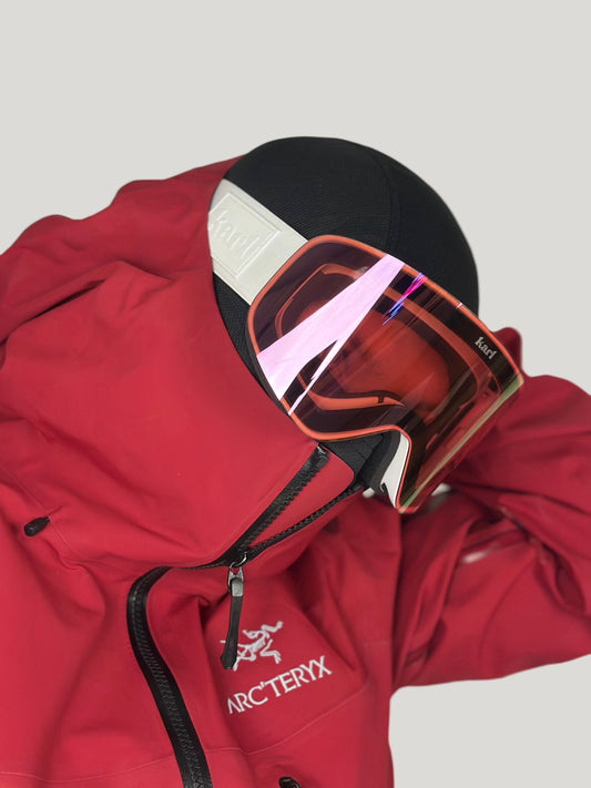 Red jacket with a hood and white goggles with pink lens on a neutral background